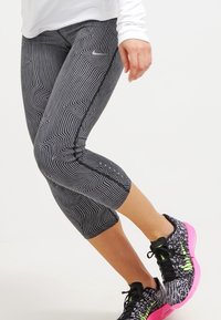 Los leggins capri con estampado en blanco y negro presentan un diseño ondulado, acentuado con un logo sutil, combinados con unas zapatillas deportivas multicolores.
