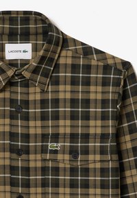 Grön och beige rutmönstrad skjorta med krage, som har svarta knappar och en liten broderad logotyp på bröstfickan.