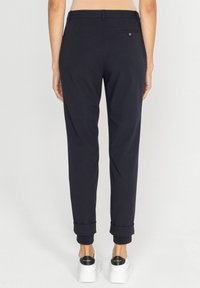 Granatowe spodnie o dopasowanym kroju, z podwiniętymi nogawkami, tylną kieszenią z guzikiem, w połączeniu z białymi trampkami na platformie.