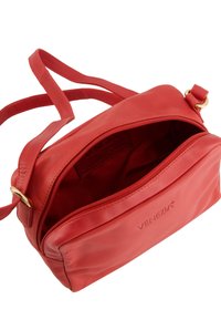 Rote Leder-Crossbody-Tasche mit einem Reißverschluss-Hauptfach und subtiler Markenkennzeichnung. Sie verfügt über eine weiche Textur und verstellbare Träger.