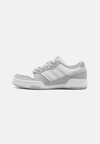Zapatillas deportivas en blanco y gris con un exterior de cuero suave, diseño de tres franjas, cuello acolchado y suela de goma texturizada.
