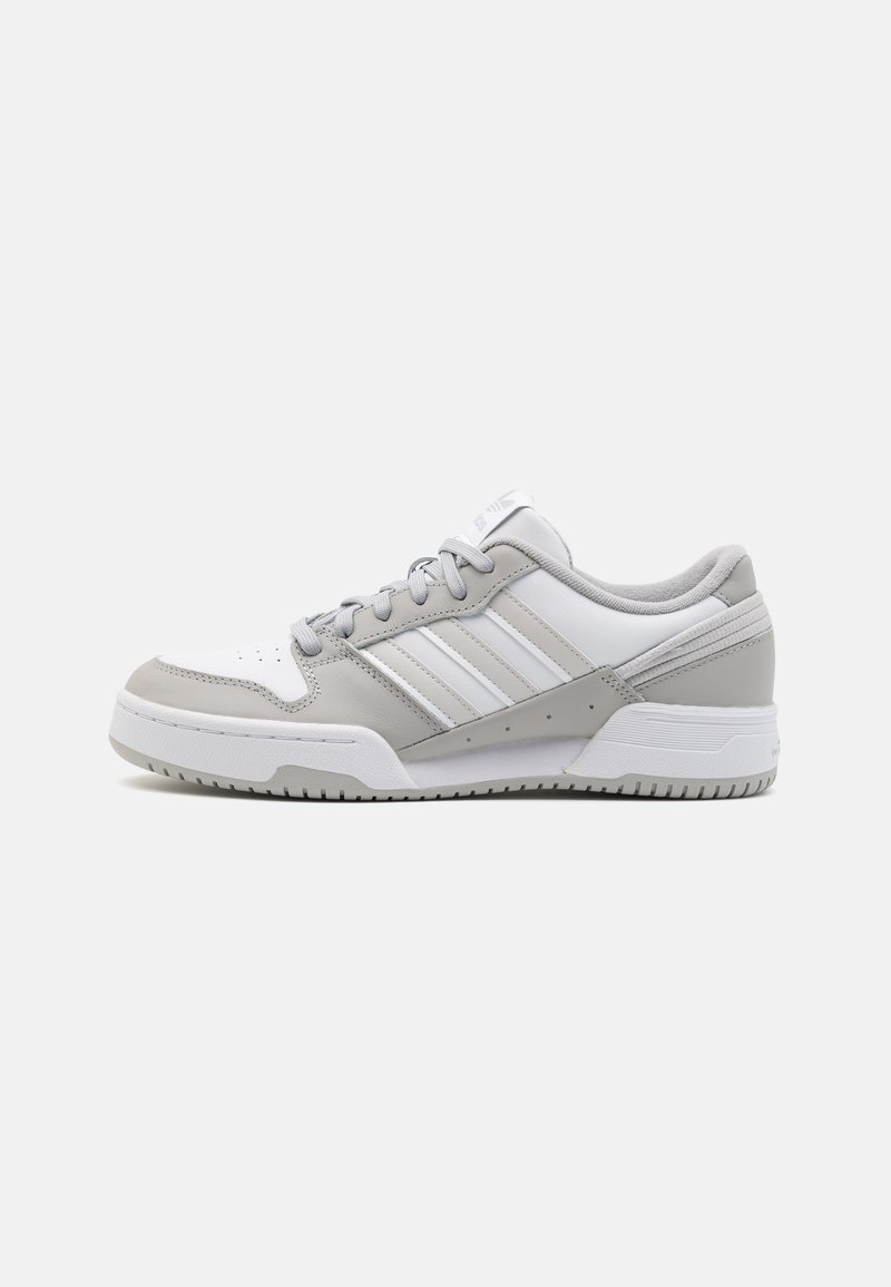 Zapatillas deportivas en blanco y gris con un exterior de cuero suave, diseño de tres franjas, cuello acolchado y suela de goma texturizada.