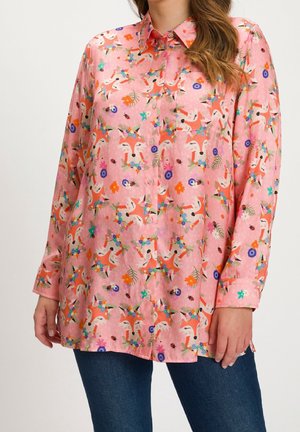 Różowa koszula na długi rękaw zapinana na guziki z kolorowymi twarzami lisów i kwiatowymi wzorami, noszona z niebieskimi dżinsami.