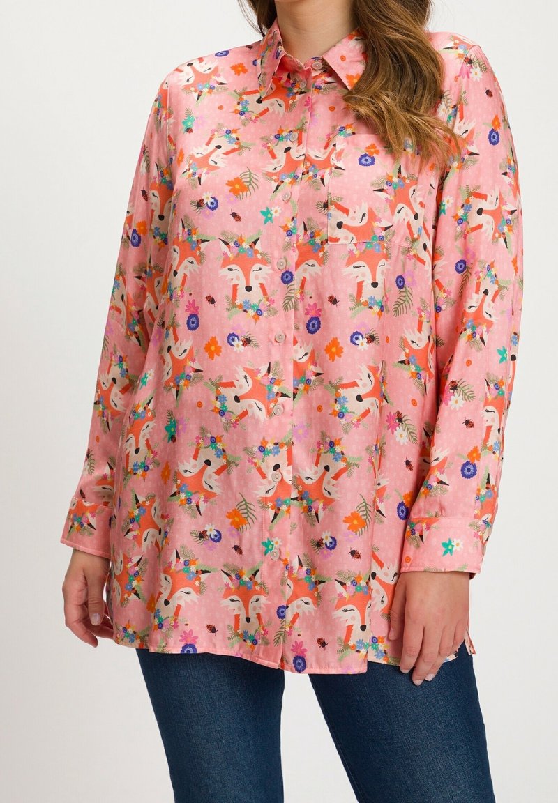 Chemise rose à manches longues avec boutons, visages de renard colorés et motifs floraux, portée avec un jean bleu.