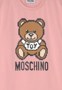 Růžová mikina se pixel art designem medvěda a nápisem "TOY" na tričku. Značka "MOSCHINO" je vytištěna níže tučnými černými písmeny.