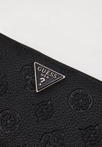 Portafoglio in pelle nera testurizzata con design in rilievo e una placca triangolare in argento con la scritta "Guess USA."