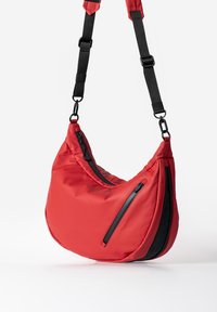 Rote Nylon-Schultertasche mit geschwungener Form, ausgestattet mit zwei schwarzen Reißverschlusstaschen und einem verstellbaren schwarzen Tragegurt. Texturierte Oberfläche.