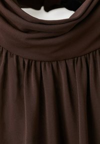 Gros plan sur un tissu côtelé brun foncé avec des plis froncés sous un col roulé plié.