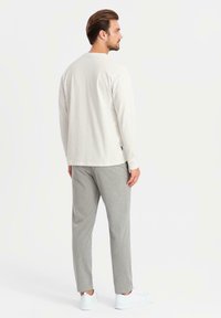 Maglietta a maniche lunghe crema abbinata a pantaloni grigi testurizzati e sneakers bianche. Design minimalista, vestibilità rilassata e palette di colori semplice.