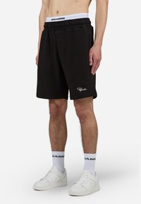 Pantaloni scurți negri cu un model texturat și un tiv elastic, având brandingul "PEGADOR". Accentuati cu broderie albă a logo-ului pe margine.