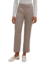 Pantalons beiges à coupe droite avec une texture lisse, taille haute et des détails de couture subtils. Associés à des mocassins blancs.