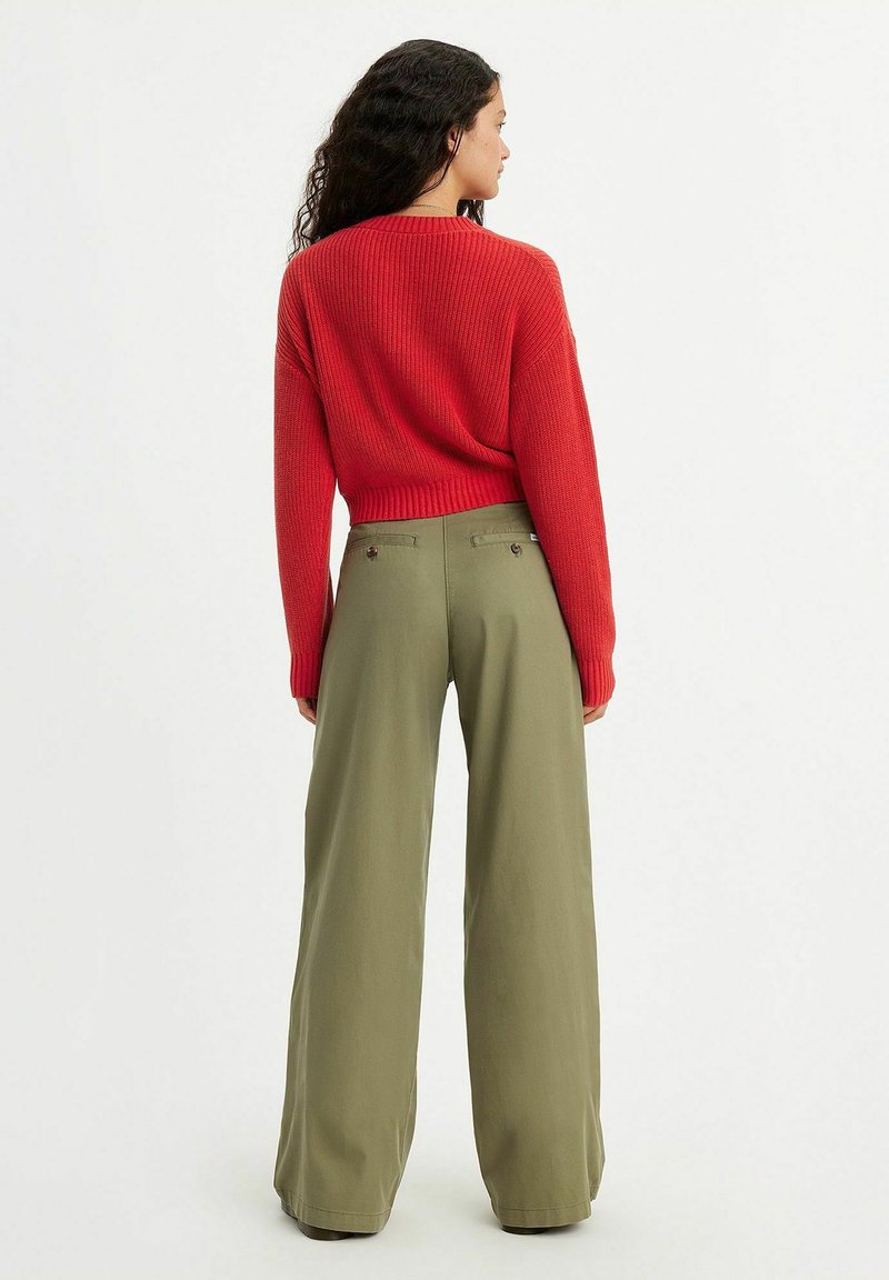 Un pull rouge côtelé à manches longues associé à un pantalon taille haute en olive avec des jambes larges. Présente un design cropped et des poches arrière.