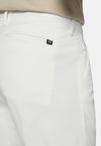 Pantalons en coton blanc avec une texture lisse, dotés d'une poche arrière et d'un petit logo bleu marine. Coupe ajustée avec un design épuré.