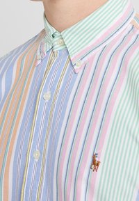 Camicia con colletto caratterizzata da righe verticali in azzurro chiaro, verde, rosa e arancione, con accenti bianchi e un piccolo logo di cavallo ricamato.