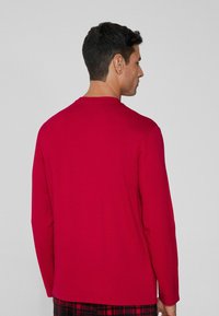 Camiseta de manga larga roja, hecha de una tela suave, con cuello redondo y un corte holgado, sin patrones visibles ni detalles adicionales.