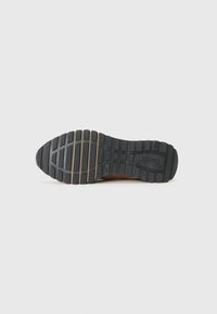 Semelle de chaussure avec une bande de roulement en caoutchouc noir comportant des rainures horizontales et verticales, et le nom de la marque « Gabor » embossé près du talon.