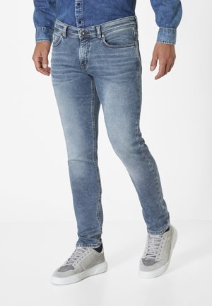 Light blue denim jeans with a slim fit, featuring whiskering effects, five pockets, and contrasting stitching, paired with gray sneakers.