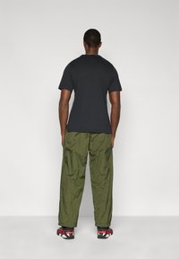 Μαύρο βαμβακερό μπλουζάκι, φαρδιά γραμμή, σε συνδυασμό με ελαφρύ παντελόνι ελιάς-πράσινου χρώματος. Τα υποδήματα έχουν κόκκινο και μαύρο σχέδιο με υφασμένους πάτους.