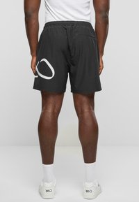 Sorte shorts med elastisk talje og en baglomme, prydet med et stort hvidt logo på venstre side. Lavet af glat, letvægtsstof.