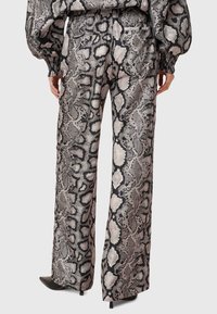 Pantalons à larges jambes avec un imprimé serpent noir et beige, présentant une texture lisse et deux poches arrière. Conçus avec une taille élastique.