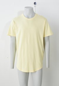 Geltonas medvilninis marškinėlis su trumpomis rankovėmis, apvalia iškirpte, laisvo silueto, lygiu paviršiumi ir apvalia apačia. Pateiktas ant pilkos spalvos manekeno.