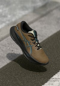 Brauner Sportschuh mit schwarzen und türkisfarbenen Akzenten, strukturierter Oberseite und gepolsterter Sohle. Mit Gore-Tex-Branding und stylischen Schnürsenkeln.