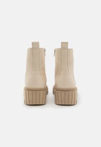 Bottines beige avec une finition lisse, pointes rondes et semelles épaisses à nervures. Elles sont dotées d'une fermeture éclair de chaque côté et d'une petite languette à l'arrière.