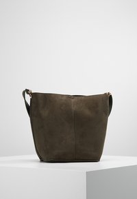 Skuldertaske i olivengrønt ruskind med minimalistisk design, blød tekstur og justerbar skulderrem. Har diskret lodret sømdetalje.