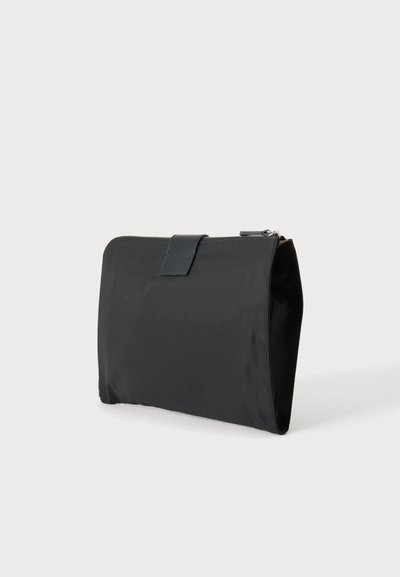 Trousse rectangulaire noire avec fermeture éclair et rabat, debout sur un fond clair uni.