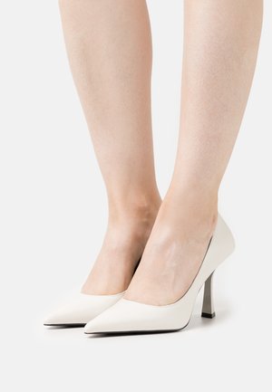 Chaussures à talons hauts en cuir blanc avec des pointes effilées et un design épuré. Les talons sont étroits et présentent un accent géométrique.