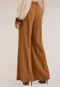 Brede broek in een gestructureerde roestkleur, met verticale strepen en een elastische tailleband. Draag het met bruine hakken.