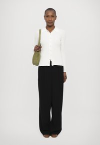 Witte cardigan met lange mouwen en knopen, gecombineerd met zwarte wijde broek en een kleine groene tas. Eenvoudig ontwerp, zonder patronen.