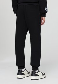 Czarne dresy ze zwężającymi się nogawkami, z tylną kieszenią i gładką teksturą, w połączeniu z czarno-białymi trampkami.