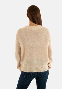 Suéter de punto beige con un ajuste relajado, mangas largas y dobladillo acanalado. Fabricado en hilo suave y peludo, con una textura ligeramente transparente.