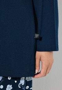Camisa de manga larga en color navy, confeccionada con una tela suave, que presenta una abertura lateral y una pequeña etiqueta de la marca en el dobladillo. Diseño texturizado y de corte relajado.