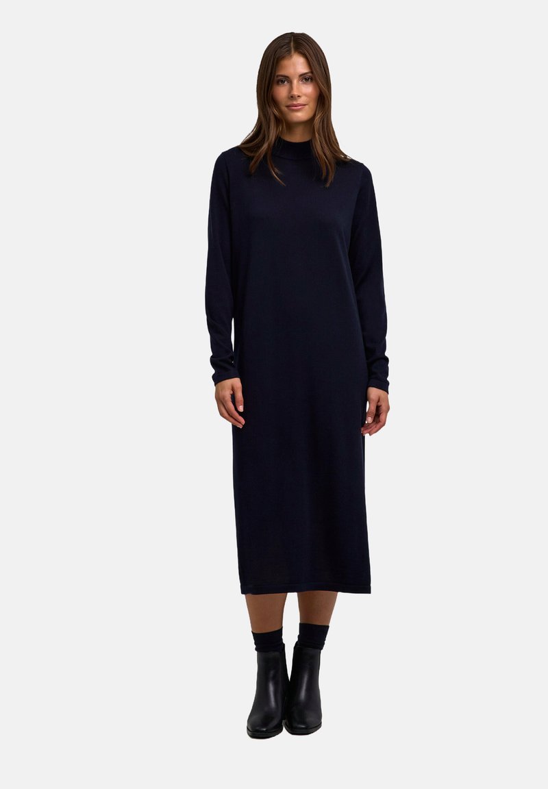 Langärmliges, marineblaues Kleid mit geradem Schnitt und Rundhalsausschnitt, aus weichem Material. Getragen mit schwarzen Stiefeletten. Einfaches Design, ohne Muster.