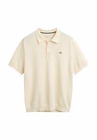 Polo-Shirt in Cremefarbe, aus strukturiertem Strickstoff. Mit klassischem Kragen, Dreiknopfverschluss und gesticktem Logo auf der Brust.