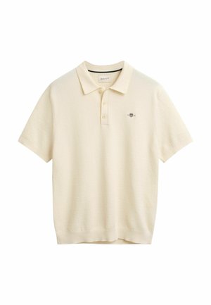 Polo in colore crema, realizzato in tessuto a maglia testurizzata. Presenta un colletto classico, una chiusura con tre bottoni e un logo ricamato sul petto.