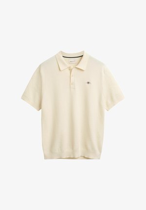 Polo-Shirt in Cremefarbe, aus strukturiertem Strickstoff. Mit klassischem Kragen, Dreiknopfverschluss und gesticktem Logo auf der Brust.