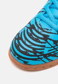 Zapatilla deportiva azul brillante con una superficie texturizada que presenta patrones en espiral negros, suela de goma marrón y cordones azules.