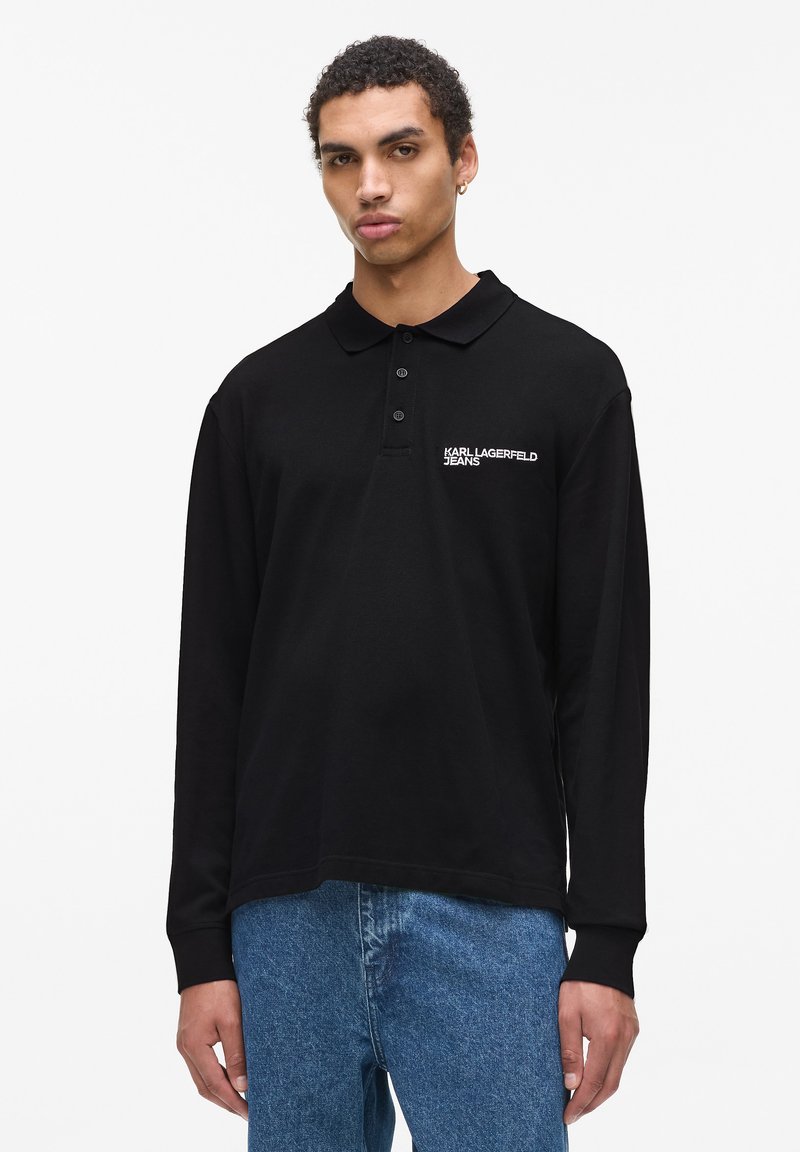 Črna polo srajca z dolgimi rokavi in ovratnikom, z vezenim logotipom "KARL LAGERFELD JEANS" na levem prsnem delu. Narejena iz gladkega materiala.