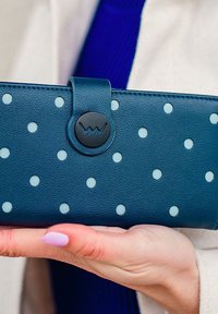 Teal leather wallet with white polka dots and a round black button closure featuring a logo. Smooth texture with stitched edges.