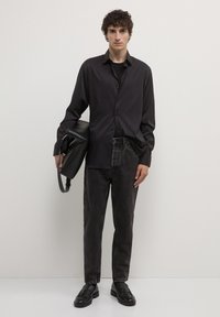Camicia nera a maniche lunghe, abbinata a jeans di denim scuri e sbiaditi. Borsa a tracolla nera in pelle, indossata sulla spalla. Mocassini neri.