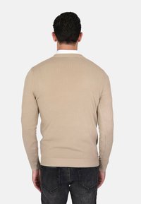 Maglione beige a maglia con scollo rotondo, polsini e orlo a costine, e una texture liscia, visto da dietro su uno sfondo semplice.