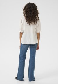 Blusa bianca a maniche puff con tessuto testurizzato, abbinata a jeans a gamba ampia blu. La blusa presenta maniche arricciate e una vestibilità rilassata.