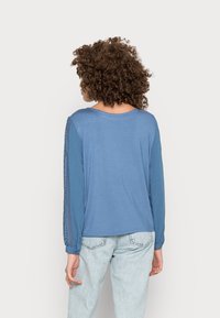 Camisola azul de mangas longas com um corte solto, com detalhes em renda ao longo das mangas e um decote em forma de U. Tecido suave com uma textura lisa.