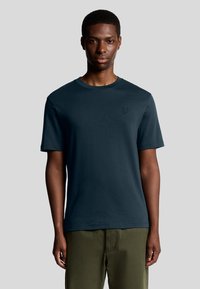 Mørkeblå kortærmet t-shirt med rund hals og et diskret broderet logo på brystet. Glat stof og afslappet pasform.