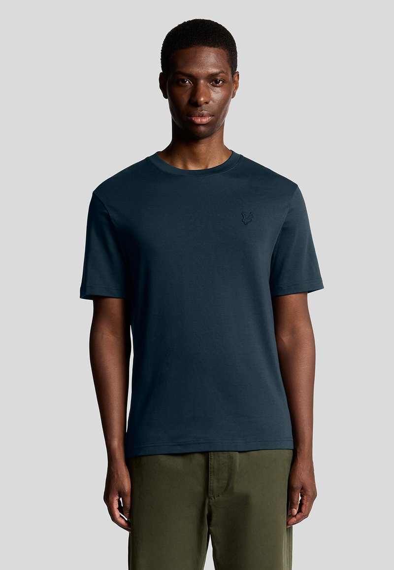 Mørkeblå kortærmet t-shirt med rund hals og et diskret broderet logo på brystet. Glat stof og afslappet pasform.