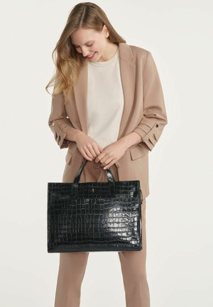 Czarna skórzana torba tote z wzorem krokodyla, wyposażona w dwie górne rączki i ustrukturalizowany design. Modelka trzyma torbę na neutralnym tle.