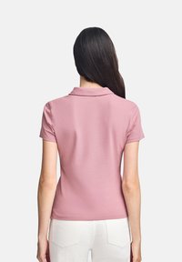 Kortärmad polo i mjuk rosa tyg, med klassisk krage och figursydd design. Bakifrån med slät textur och enkel styling.